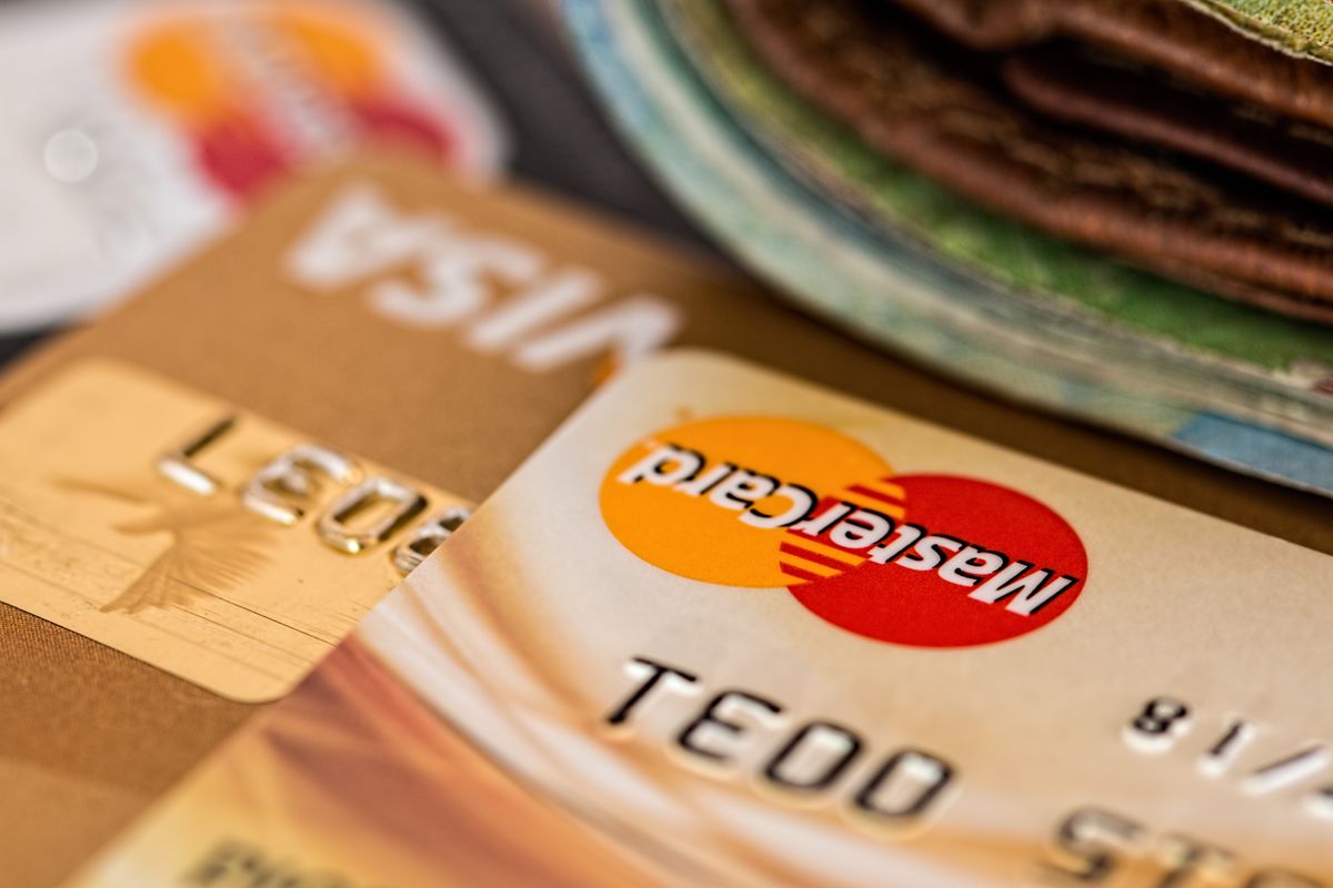 A close-up of stacked credit cards (Visa, Mastercard) and bundled banknotes in the background, illustrating the salary and compensation topic