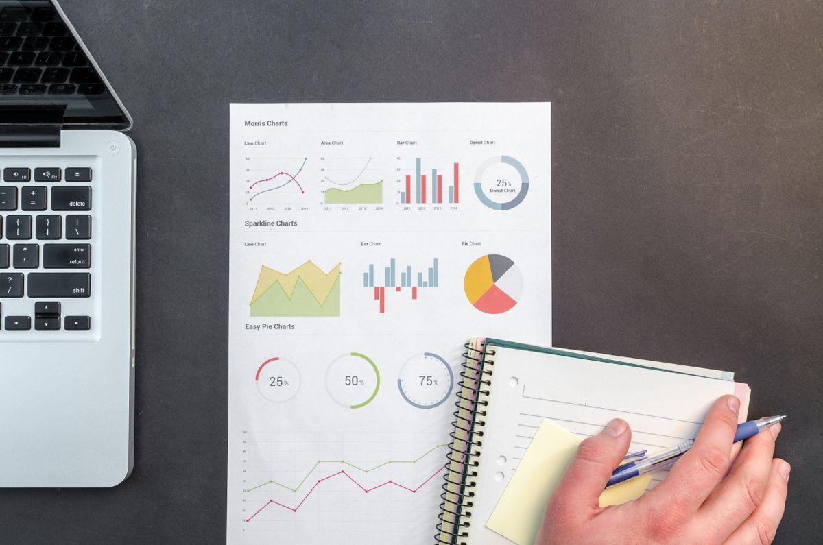Flat lay of a workspace with a laptop, printed chart mockups, and a notebook — typical data analysis setup for practicing SQL queries