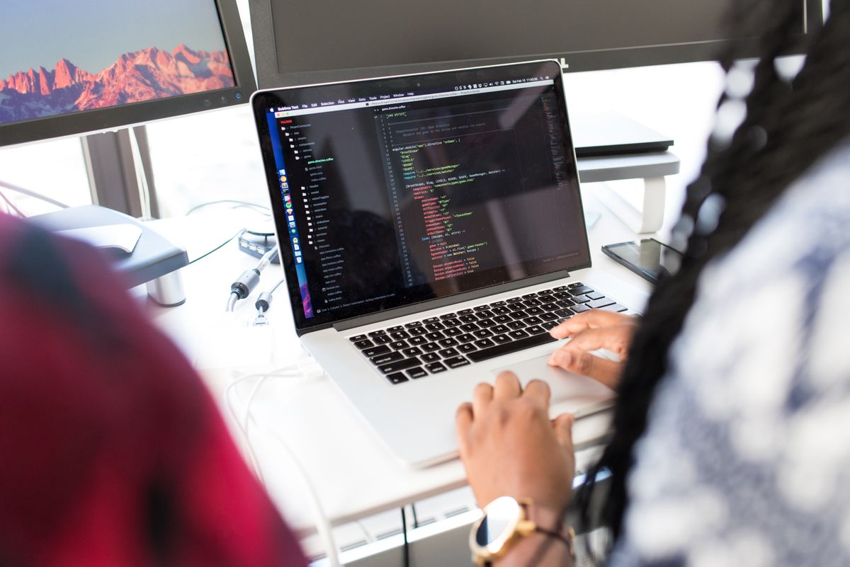A developer working in a code editor on a laptop, with colorful syntax-highlighted code visible on the screen — the typical environment for writing Python and pandas scripts
